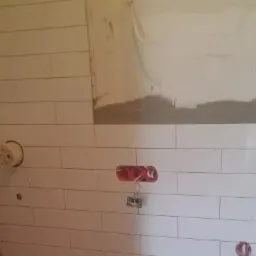 Ściana w trakcie układania białych, podłużnych płytek w Kościerzynie, widoczne puszki elektryczne i fragment ściany przygotowany pod dalsze prace.