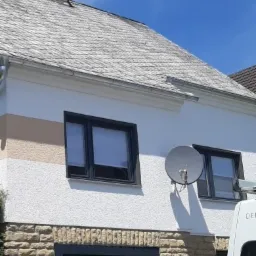 Elewacja domu z dwoma oknami w ciemnych ramach, satelita na ścianie, dach pokryty łupkiem.