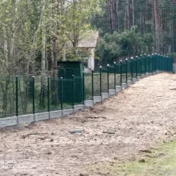 Zielone panele ogrodzeniowe z podmurówką betonową w Czersku, widok z perspektywy gruntu, z widocznymi pozostałościami po montażu i leśnym tłem.