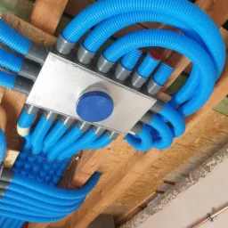 Rozprowadzenie niebieskich, karbowanych przewodów wentylacyjnych od skrzynki rozdzielczej pod drewnianym stropem.