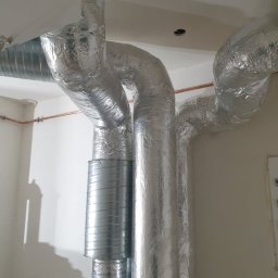 Instal HT - System rur wentylacyjnych i rekuperacyjnych, owiniętych srebrną folią izolacyjną, podłączonych do urządzenia Vaillant, z widoczną miedzianą rurką na ścianie.