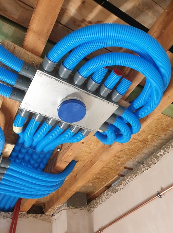 Rozprowadzenie niebieskich, karbowanych przewodów wentylacyjnych od skrzynki rozdzielczej pod drewnianym stropem.