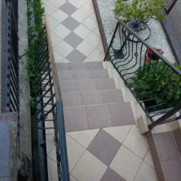 Schody zewnętrzne wyłożone płytkami w romby, z metalową balustradą i roślinnością po bokach, widok z góry.