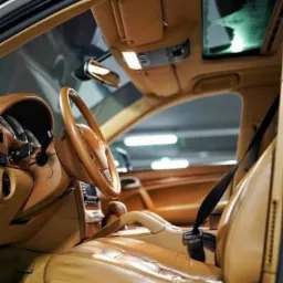 Wnętrze samochodu z jasną skórzaną tapicerką, widok na fotel kierowcy, deskę rozdzielczą i fragment dachu panoramicznego.