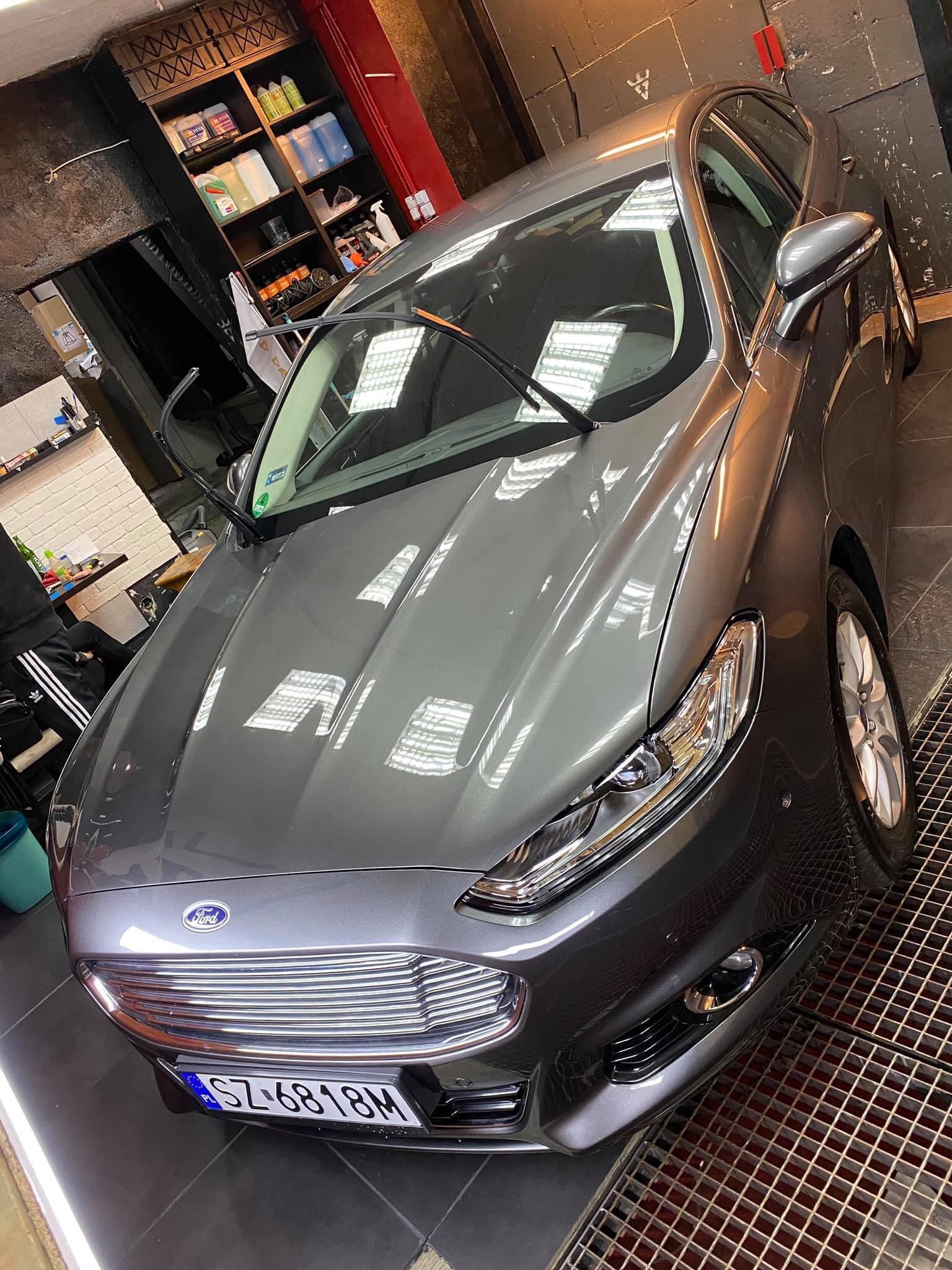 Szary Ford Mondeo po umyciu, stojący na metalowej kratce w myjni samochodowej, widoczne odbicia światła na karoserii.