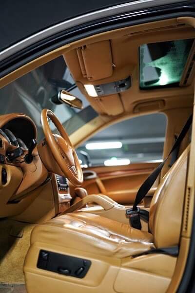 Wnętrze samochodu z jasną skórzaną tapicerką, widok na fotel kierowcy, deskę rozdzielczą i fragment dachu panoramicznego.