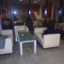 TIP TOP CLEANING SERVICES AGNIESZKA ROGAL-MOŃ - Wnętrze biurowe w Kołobrzegu po sprzątaniu: jasne sofy, szklany stolik, duże okna. Widoczne odbicia w szybach. Czysta podłoga z płytek.