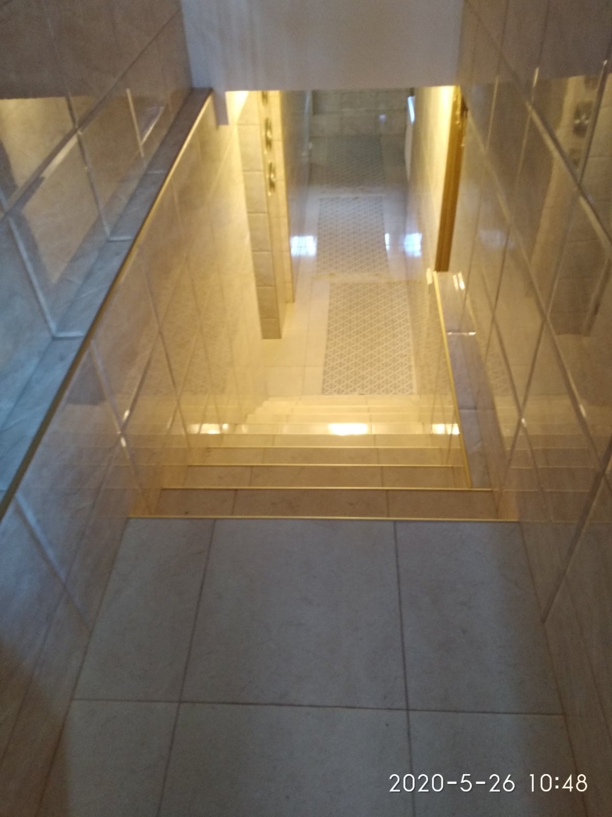 Wykończone schody wewnątrz budynku, wyłożone jasnymi, kwadratowymi płytkami ceramicznymi na ścianach i podłodze, z widocznym fragmentem korytarza w tle.