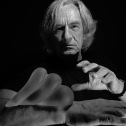 Saj Photography - Czarno-białe portretowe ujęcie starszego mężczyzny z silikonowymi implantami piersi na dłoni, oświetlonymi z boku, na ciemnym tle.