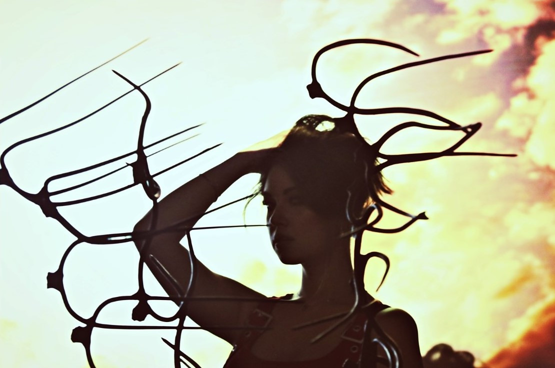 Kobieta we Wrocławiu pozuje na tle nieba, z włosami upiętymi ręką i ozdobami z drutu wokół głowy, tworzącymi artystyczny efekt.