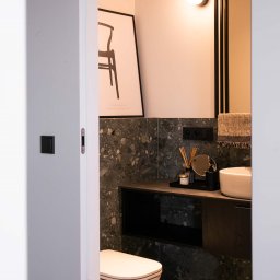 2 RAZY K - Nowoczesna, mała łazienka z umywalką nablatową, toaletą i dekoracyjną grafiką. Ciemne płytki imitujące kamień i minimalistyczne oświetlenie.