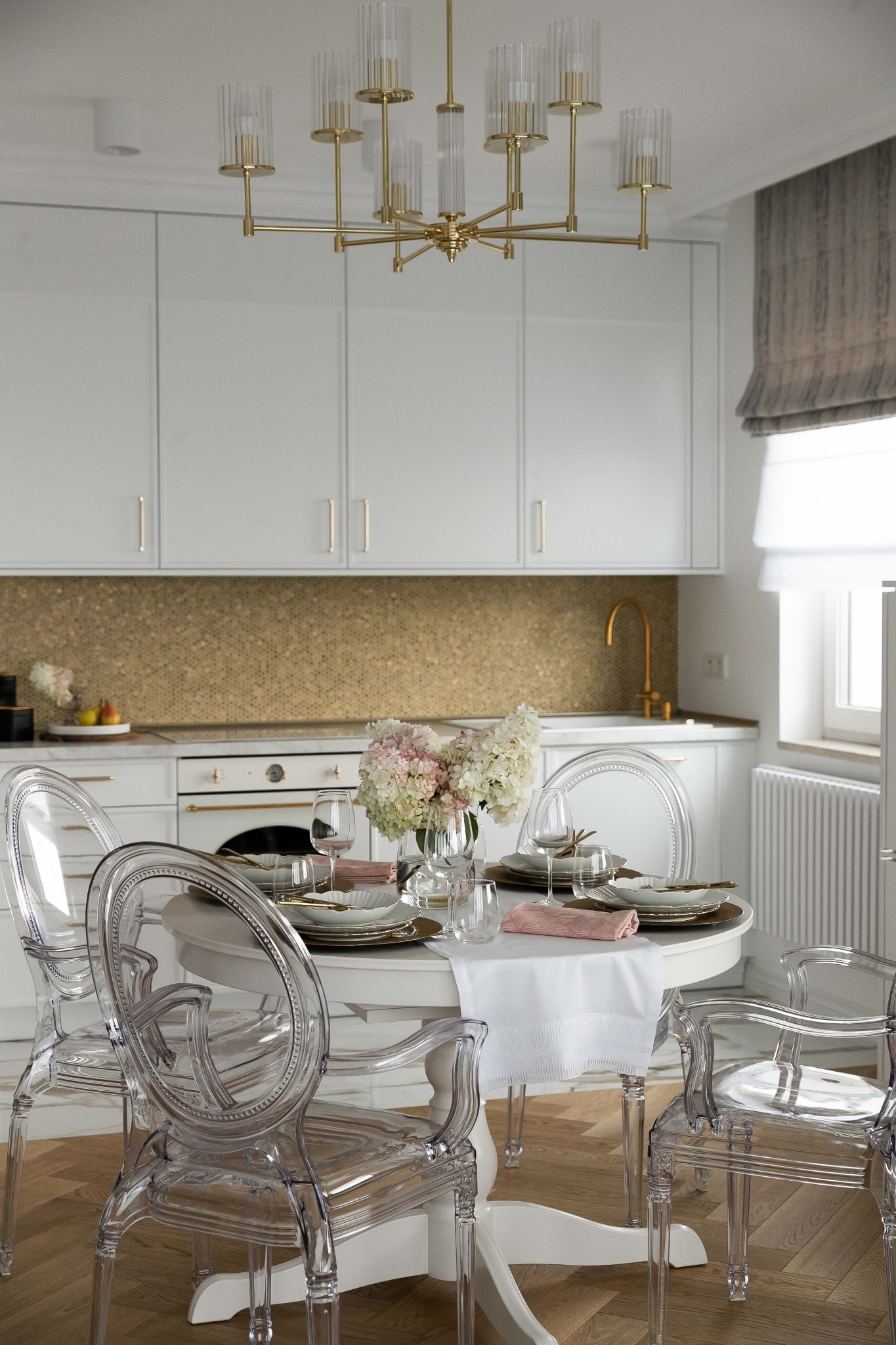 Elegancka aranżacja jadalni w jasnych kolorach z okrągłym stołem, przezroczystymi krzesłami w stylu Ludwika XVI, złotym żyrandolem i mozaiką na ścianie w tle.