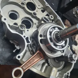 Rozłożony silnik motocyklowy z widocznym wałem korbowym, korbowodem z oznaczeniem HP89-1 i łożyskiem kulkowym, umieszczony na warsztatowym stole.