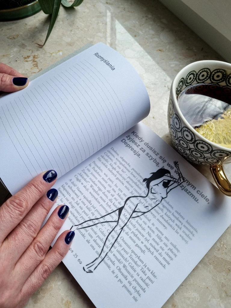 Otwarta książka z tekstem i ilustracją kobiety w ruchu, obok filiżanka z herbatą i cytryną, dłonie kobiety z ciemnym lakierem na paznokciach trzymające książkę.