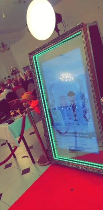 Elegancka fotobudka lustrzana z zielonymi diodami LED, czerwonym dywanem i rekwizytami na stole podczas imprezy.