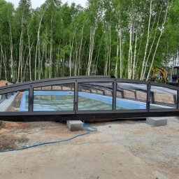 STELLER PPHU Tomasz Steller - Zadaszenie basenowe z przesuwnymi segmentami, częściowo zamontowane na betonowych bloczkach, na tle lasu brzozowego i koparki.