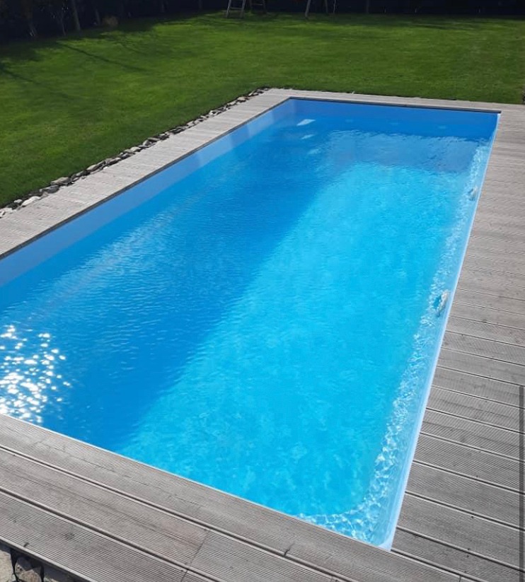 Prostokątny basen z błękitną wodą, otoczony drewnianym tarasem i zielonym trawnikiem w tle.