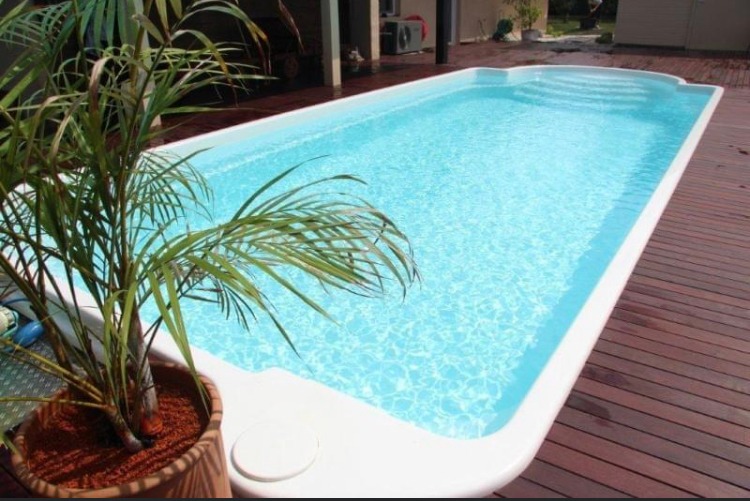 Prostokątny basen z białym obramowaniem, otoczony drewnianym tarasem, z palmą w donicy w rogu, wypełniony czystą, błękitną wodą.