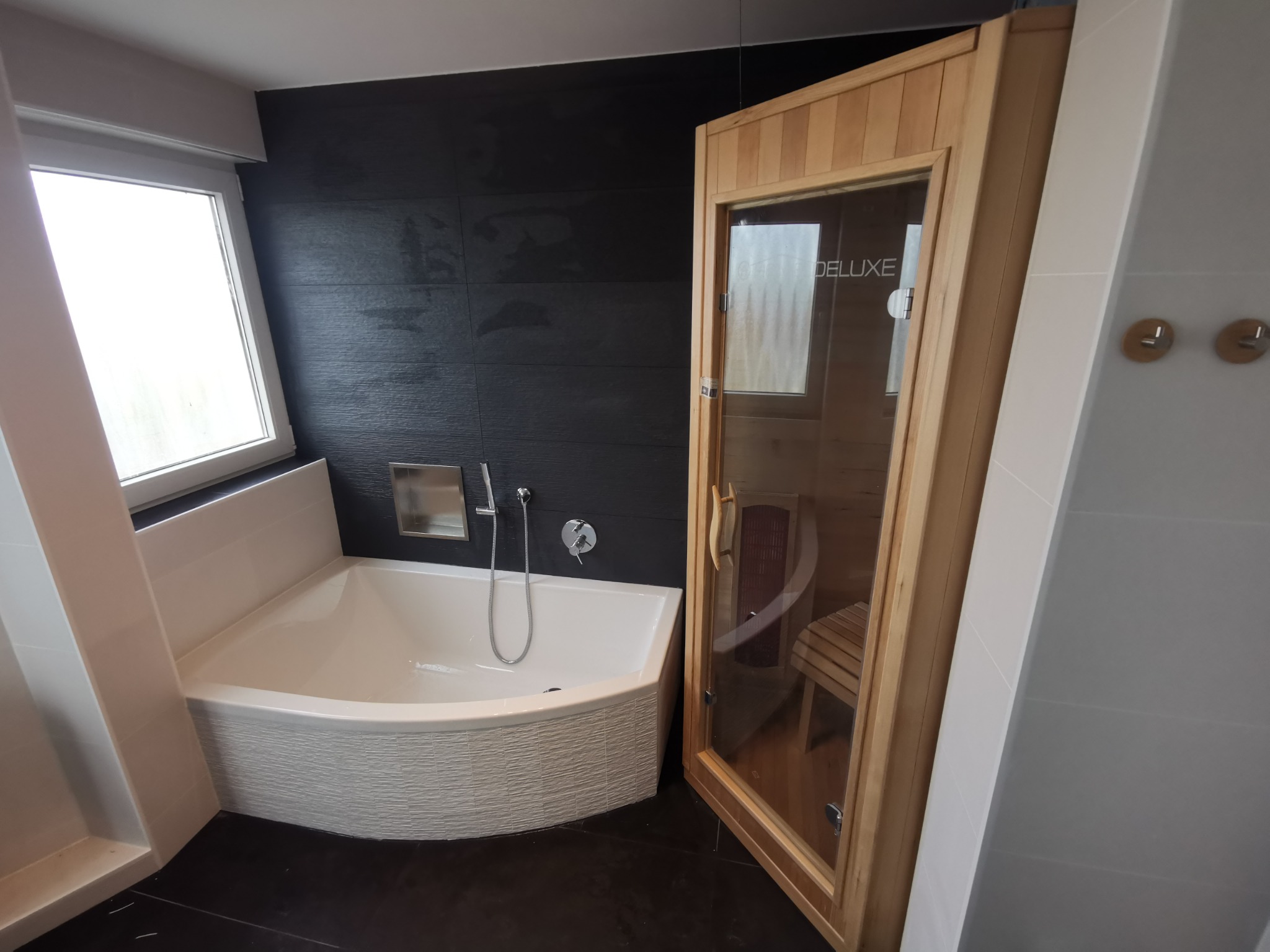 Nowoczesna łazienka z wanną o zaokrąglonym kształcie i drewnianą sauną z przeszklonymi drzwiami.