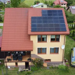 Widok z lotu ptaka na dom jednorodzinny z panelami słonecznymi na dachu i zaparkowanym obok samochodem serwisowym z otwartymi drzwiami.