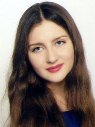 Portret młodej kobiety z długimi, brązowymi włosami, delikatnym makijażem i niebieskimi oczami, na jasnym tle.