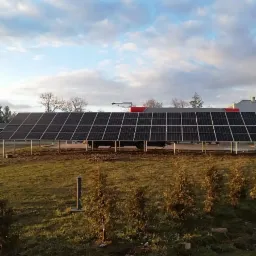 Instalacja paneli fotowoltaicznych w Sandomierzu na tle pochmurnego nieba i zielonego trawnika z młodymi drzewkami.