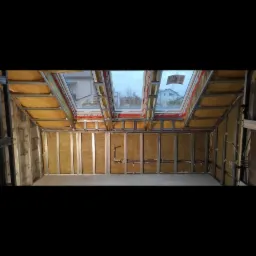 Poddasze w trakcie izolacji: widoczne metalowe profile, wełna mineralna między nimi oraz okna dachowe.