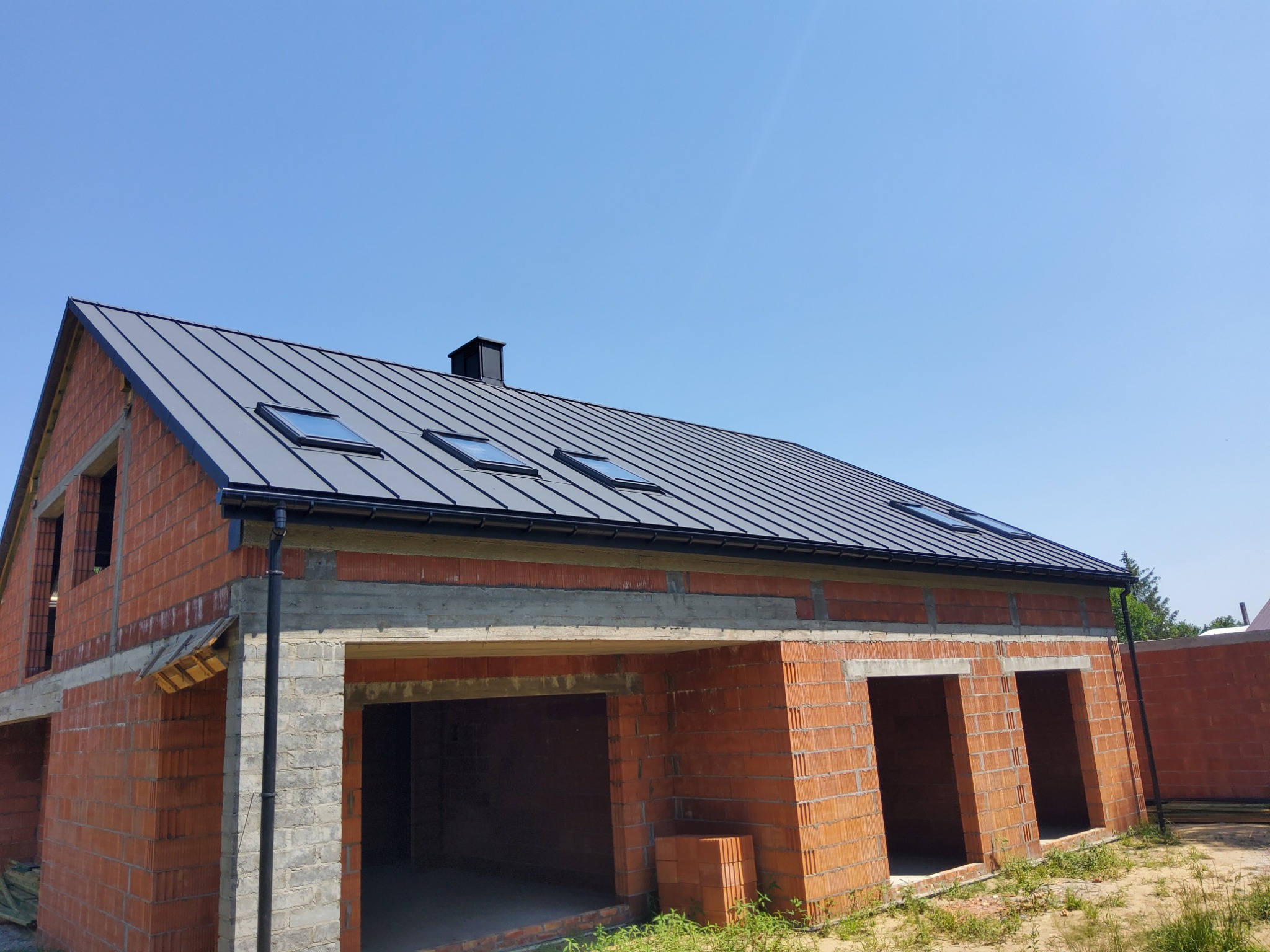 Dom w trakcie budowy z nowym, grafitowym dachem z blachy trapezowej i oknami dachowymi, widoczne rynny