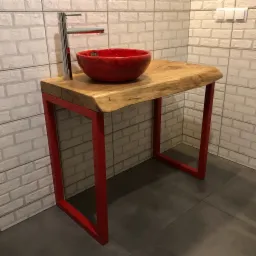Umywalka ceramiczna w intensywnym czerwonym kolorze, osadzona na blacie z naturalnego drewna o nieregularnych krawędziach, wsparta na czerwonym stalowym stelażu w łazience z białymi płytkami...