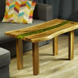 Stolik kawowy z blatem z naturalnego drewna z żywicą epoksydową w kolorze zielonym, ustawiony w salonie obok szarej sofy z kolorową poduszką.