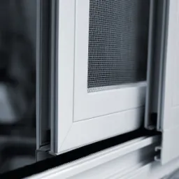 Szczegółowy widok przesuwnej moskitiery w białej ramie, widoczny mechanizm prowadnicy i siatka o drobnych oczkach.