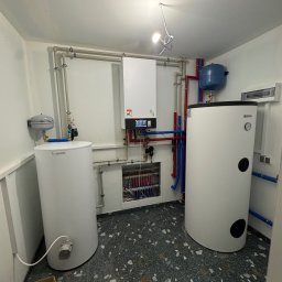 Hydraulik Pomoże - Biały piec gazowy Viessmann i zasobnik Kospel z niebieskim zbiornikiem wyrównawczym, połączone rurami w kotłowni z szarym lastryko na podłodze.