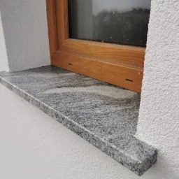 Granitowy parapet VISCOUNT WHITE zamontowany w Kielcach pod drewnianym oknem na tle białego, chropowatego tynku zewnętrznego.