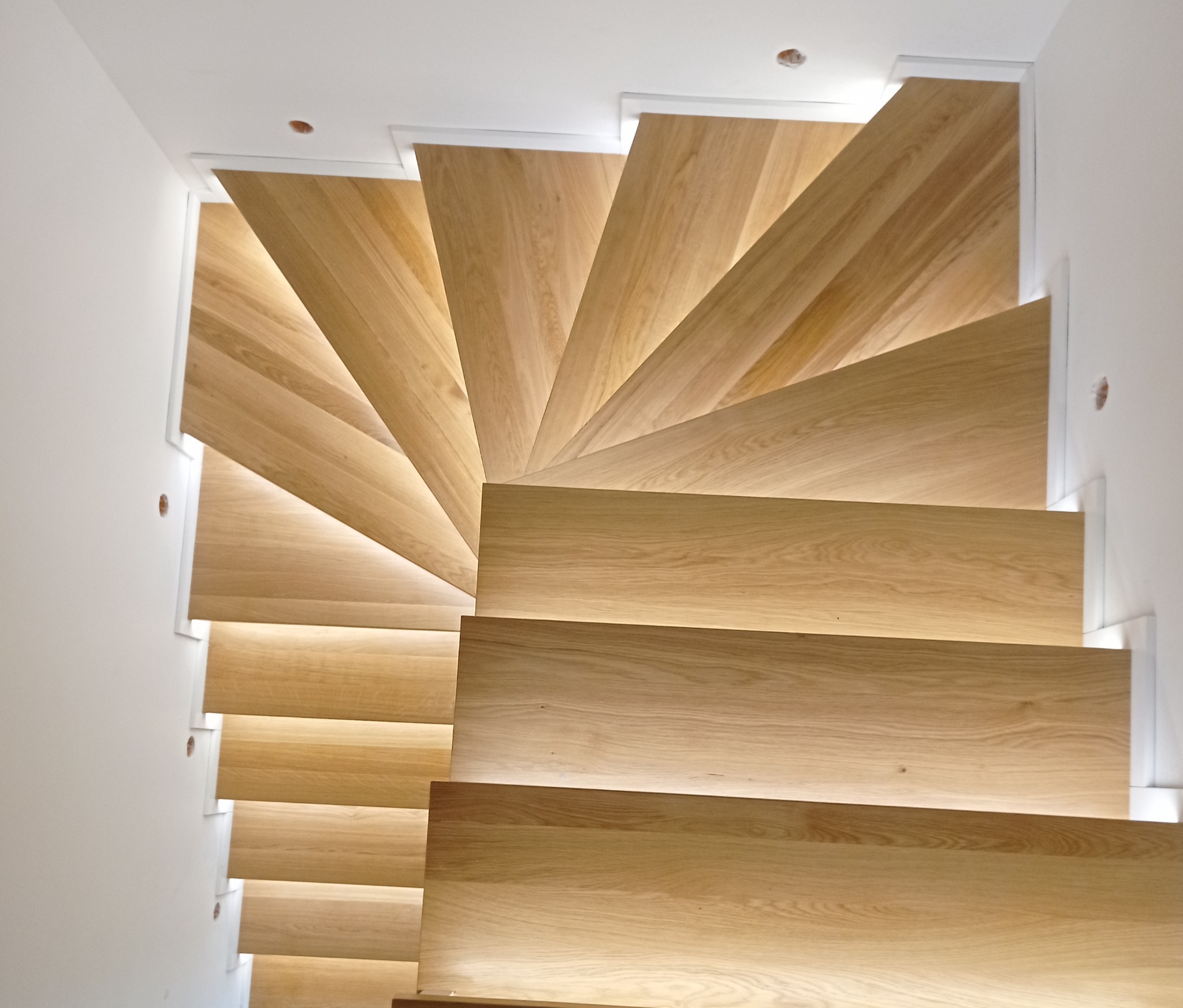 Spiralne schody drewniane z podświetleniem LED, widok z góry, minimalistyczny design, białe ściany.