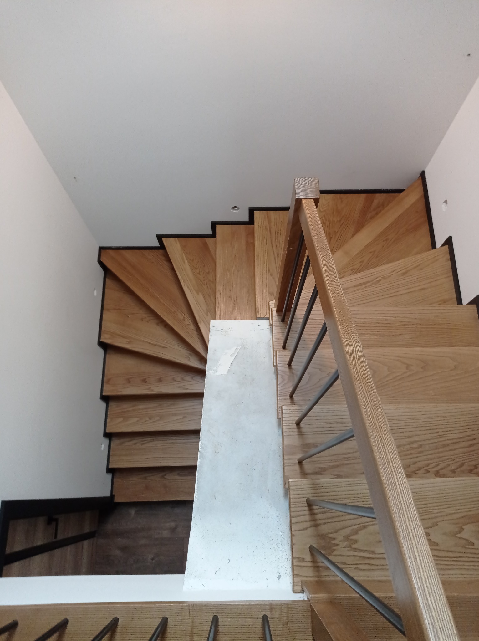 Widok z góry na drewniane schody z metalowymi balustradami, częściowo zabezpieczone folią malarską podczas remontu.