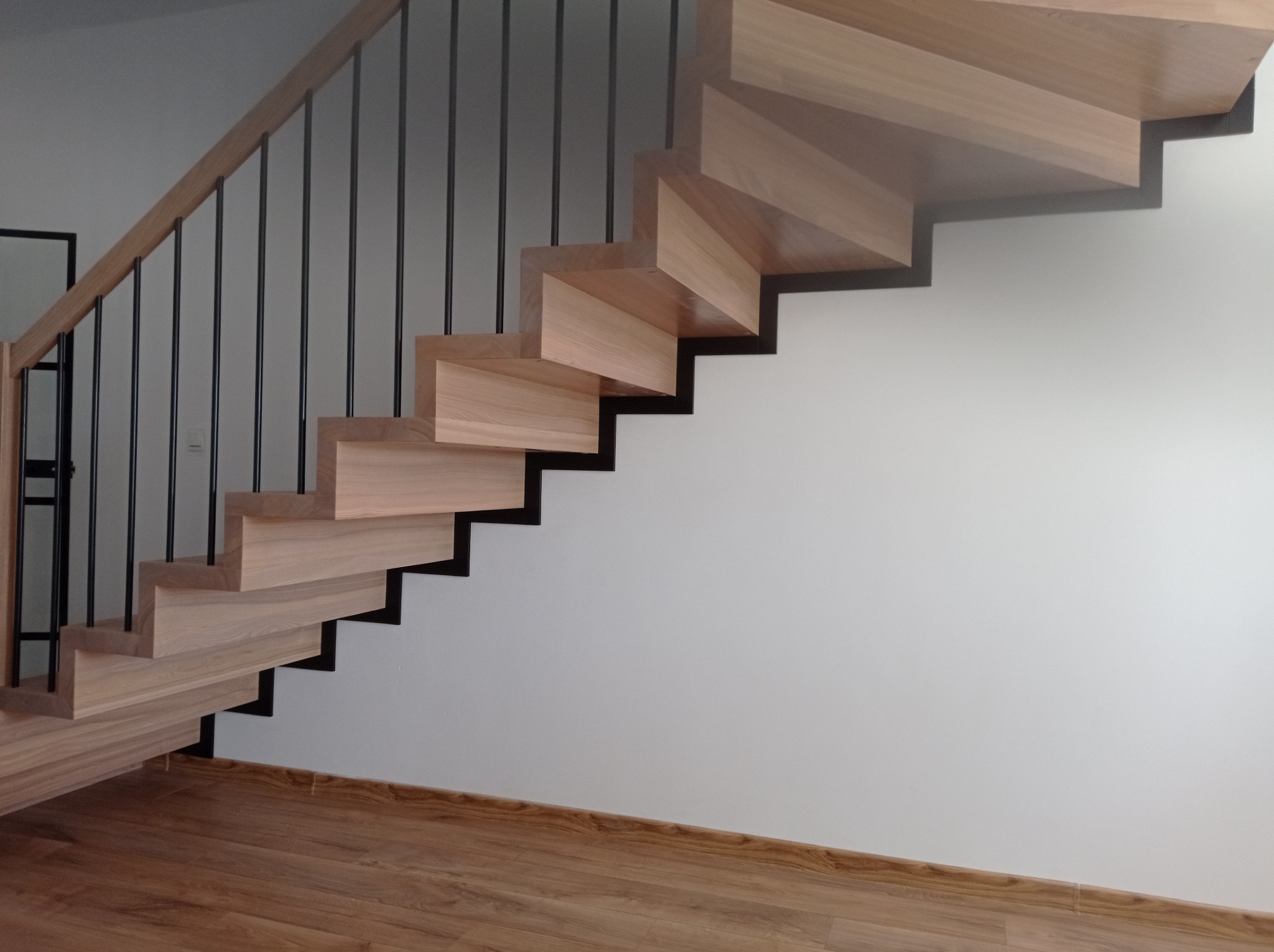 Nowoczesne schody z jasnego drewna z czarnymi metalowymi prętami balustrady, widok z dołu, minimalistyczny design.