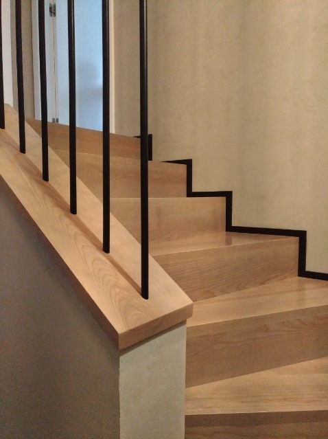 Jasne, drewniane schody z czarnymi, metalowymi balustradami we Wrześni, widoczne z dołu pod kątem.