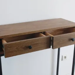Drewniana konsola z dwoma wysuwanymi szufladami na czarnych, metalowych nogach, jedna szuflada otwarta, widoczne prowadnice szuflady, minimalistyczny design, biała ściana w tle.