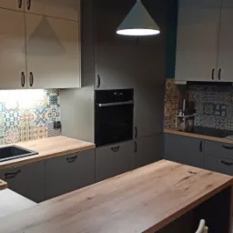 Szara kuchnia z drewnianym blatem, wzorzystymi kafelkami nad blatem i wyspą kuchenną z blatem z litego drewna.