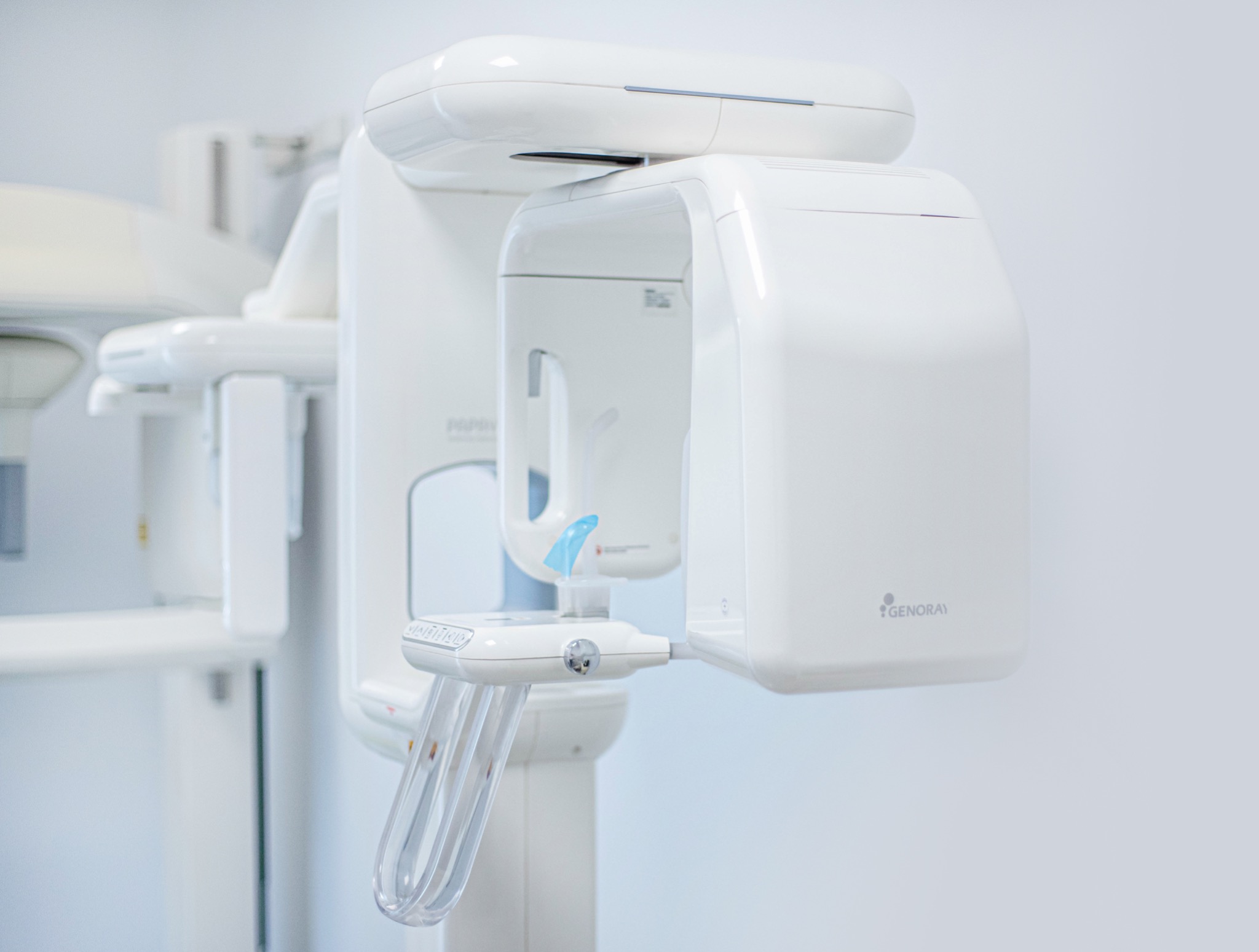 Biały panoramiczny aparat rentgenowski Genoray Papaya w gabinecie lekarskim, widoczne elementy mocujące i ramię urządzenia.