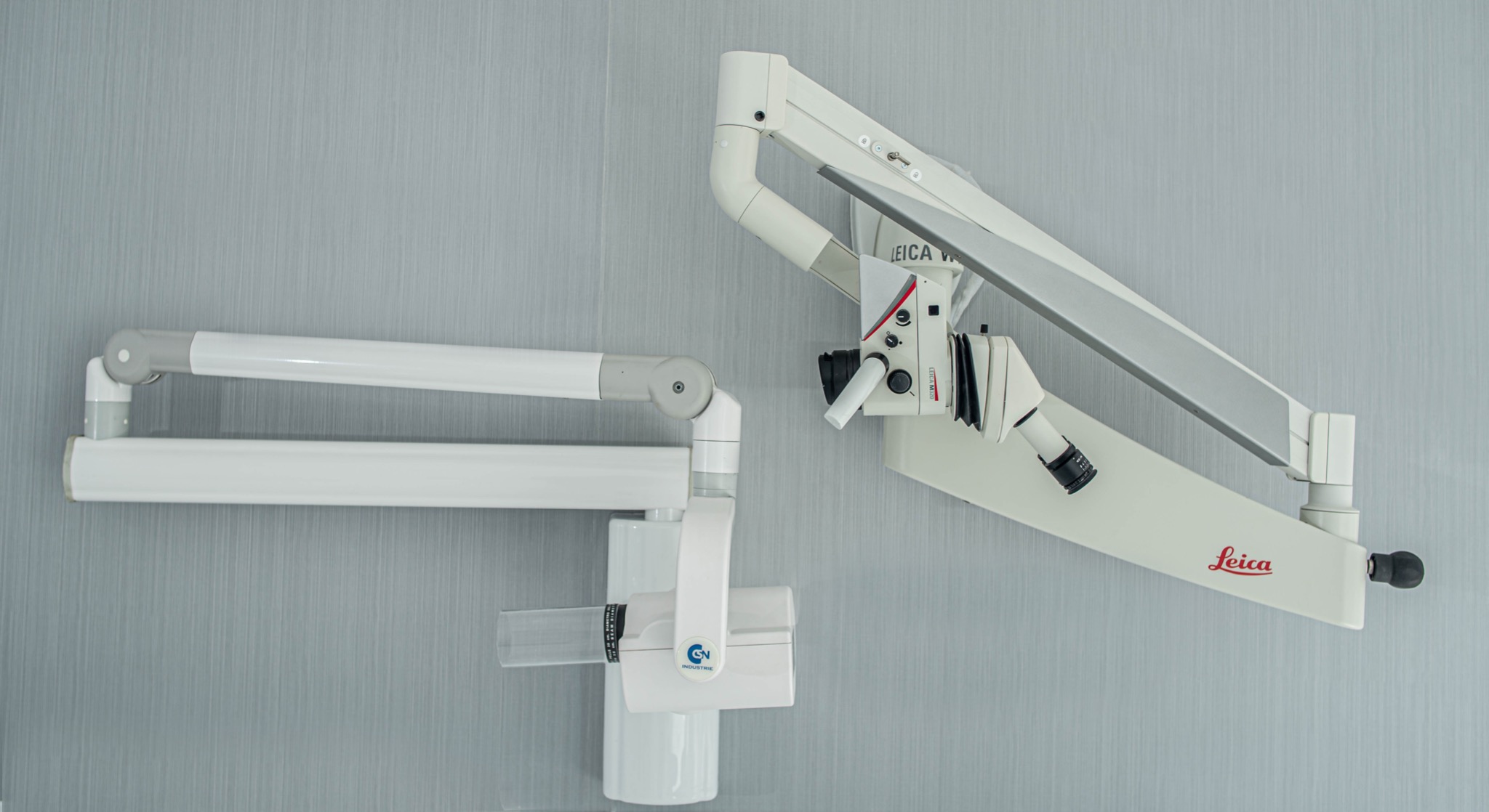 Stomatologiczny mikroskop Leica na regulowanym ramieniu oraz aparat RTG punktowy na ścianie o delikatnej fakturze.