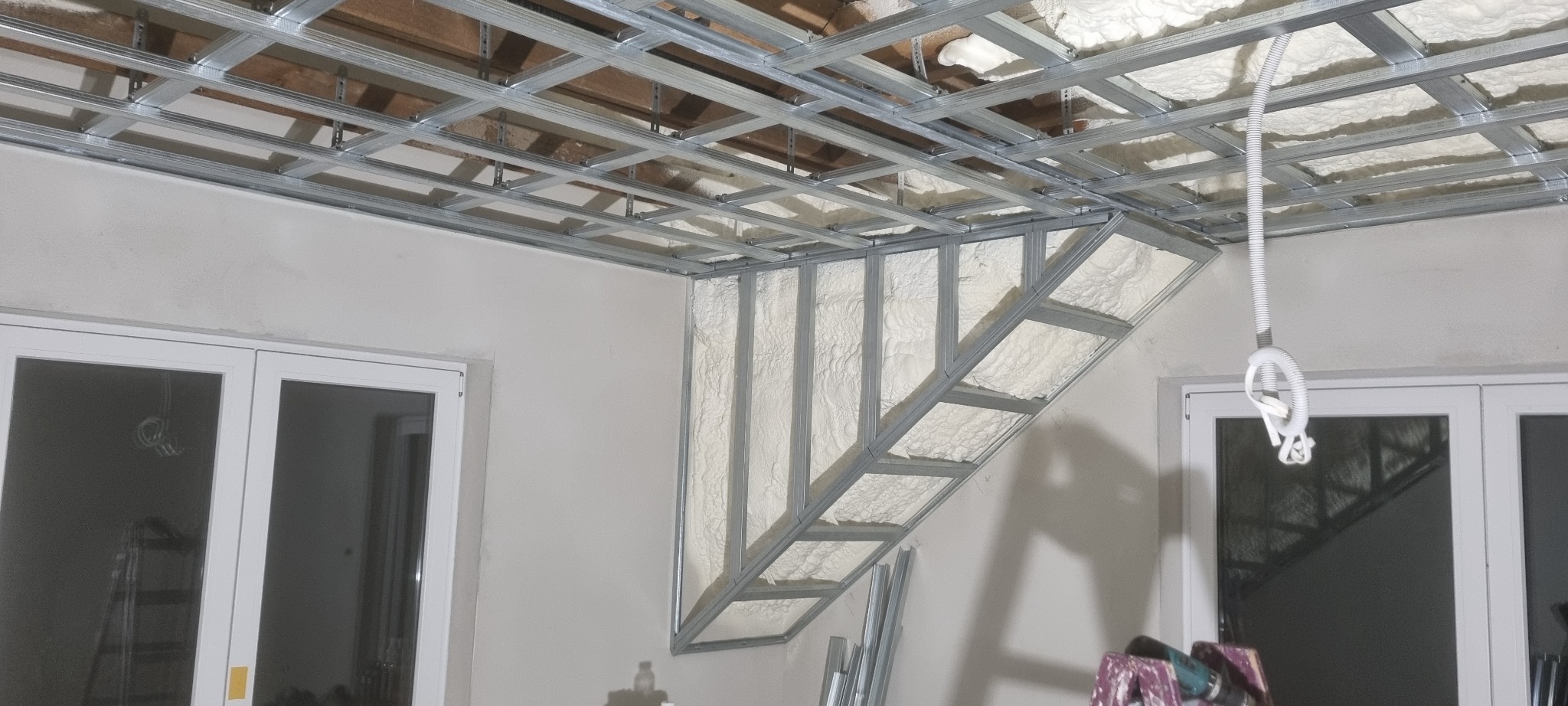 Stelaż metalowy pod zabudowę sufitu z płyt kartonowo-gipsowych, częściowo wypełniony izolacją, widok na konstrukcję z metalowych profili z fragmentem instalacji elektrycznej.