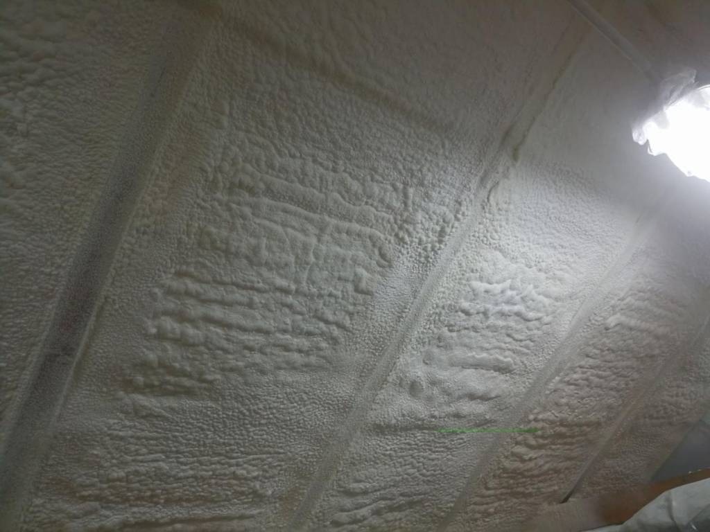 Ocieplenie poddasza pianką PUR, widoczne nierównomierne nałożenie piany i elementy konstrukcyjne dachu.