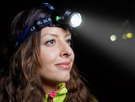 Kobieta z czołówką LED, testująca oświetlenie w Raszynie, z widocznym skupionym strumieniem światła w ciemności.