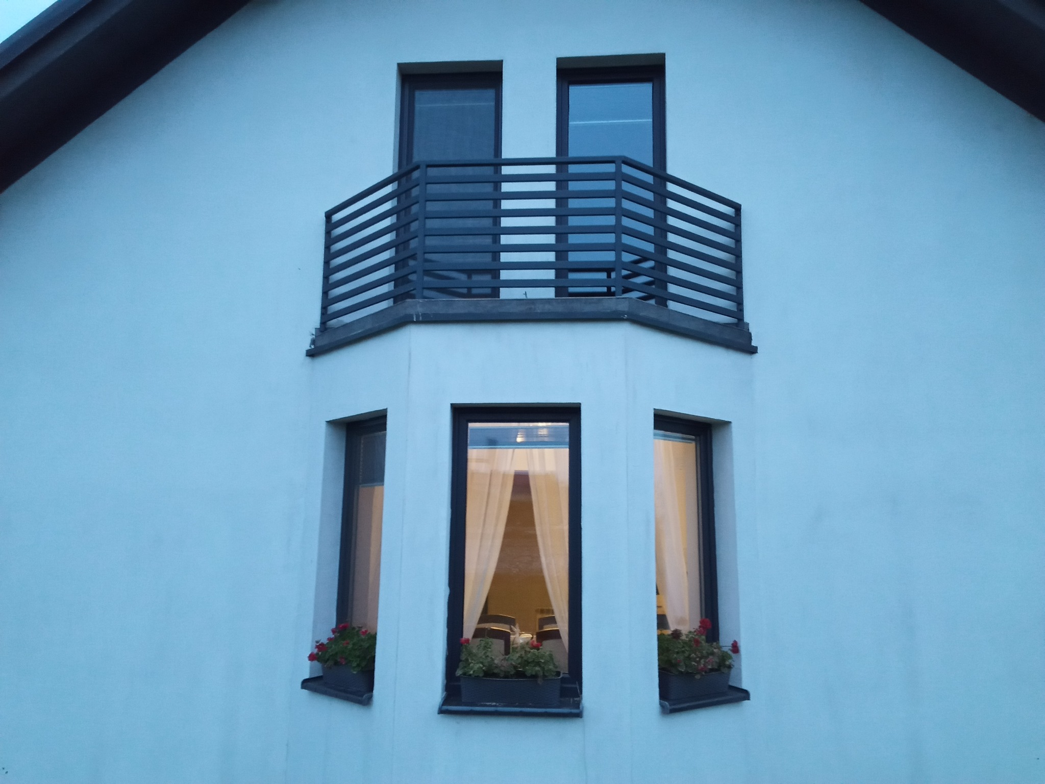 Elewacja budynku z balkonem z metalową balustradą i oknami z kwiatami w doniczkach.