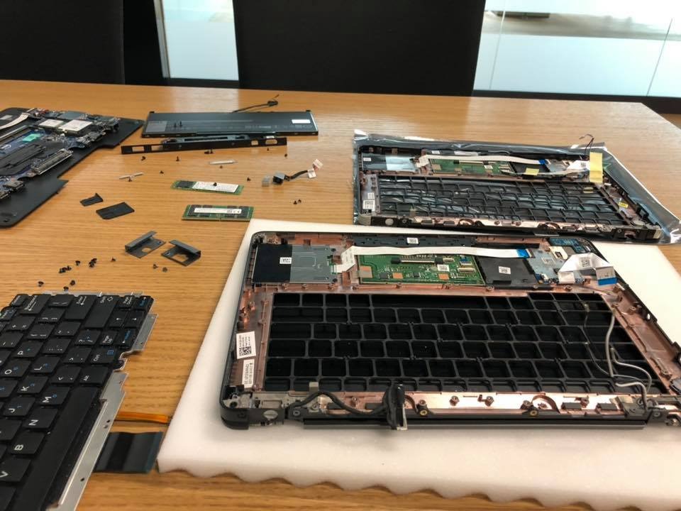 Dwa rozłożone laptopy na drewnianym stole, widoczne płyty główne, klawiatury i inne części, śrubki rozsypane obok.