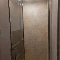 Kabina prysznicowa z deszczownicą i beżowymi płytkami ze wzorem geometrycznym na ścianach.