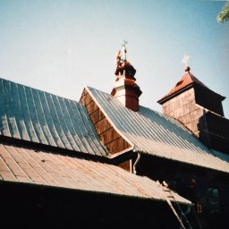 Usługi budowlane - Stary, drewniany kościół z blachy falistej na dachu i drewnianą wieżą z krzyżem, z pracownikiem na drabinie przy rynnie.