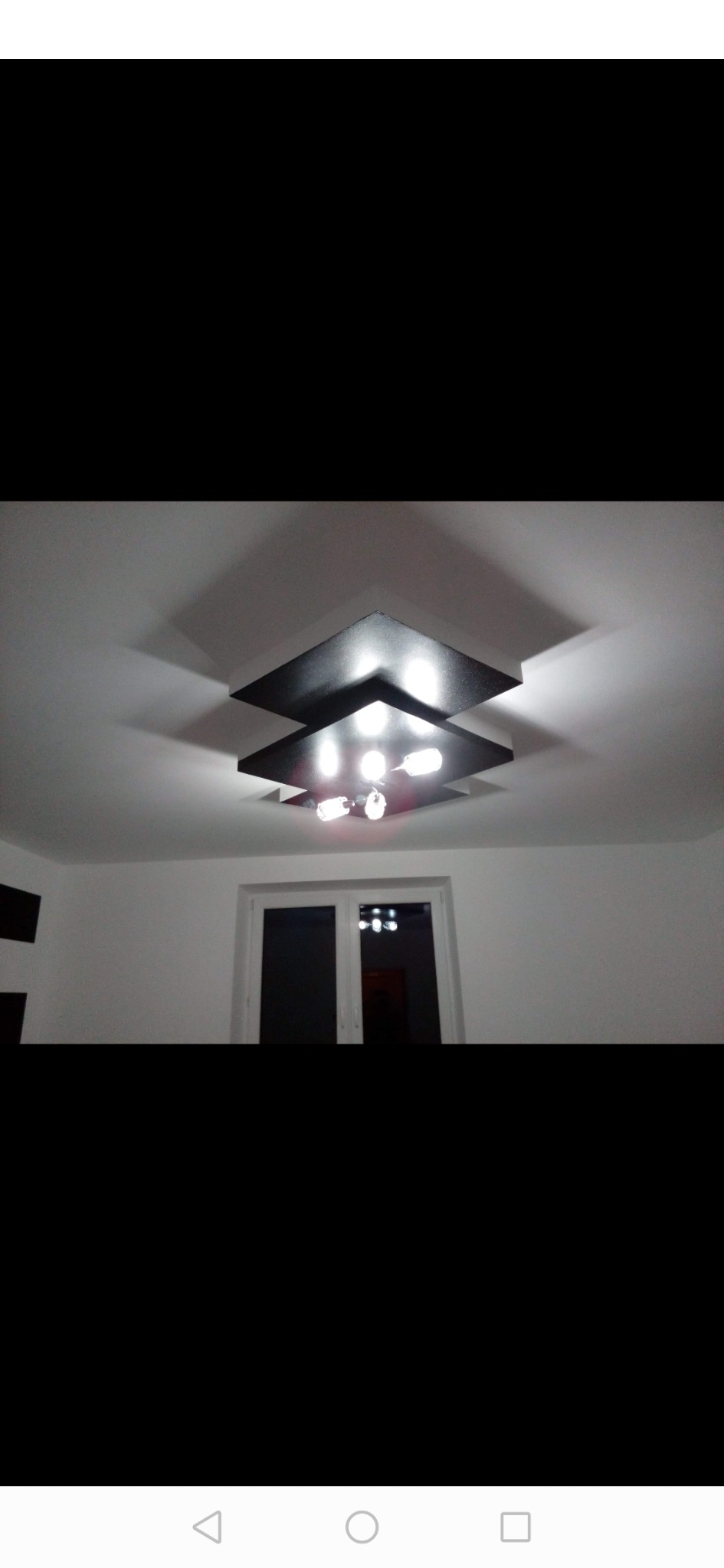 Nowoczesna, dwupoziomowa lampa sufitowa z czterema żarówkami, rzucająca geometryczne cienie na biały sufit w świeżo wyremontowanym pokoju z oknem.