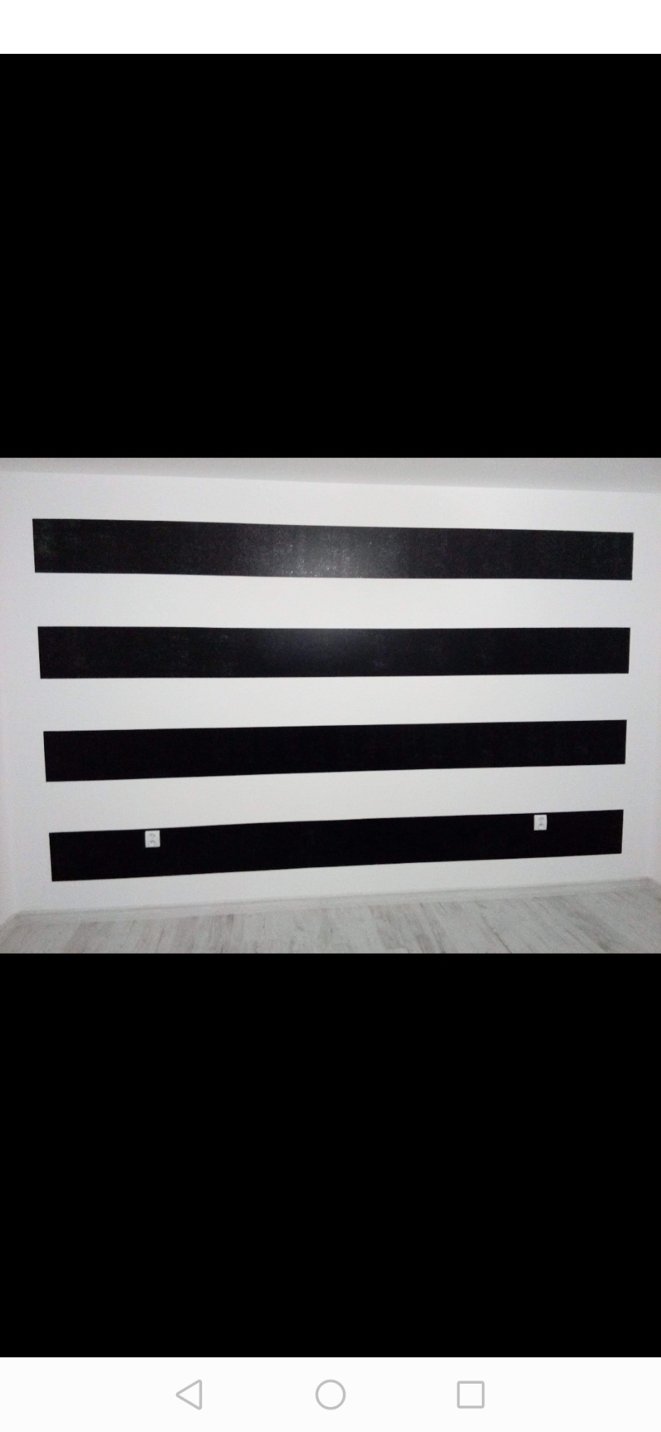 Ściana w pokoju pomalowana w poziome, czarno-białe pasy, z widocznymi gniazdkami elektrycznymi na jednej z pasów.